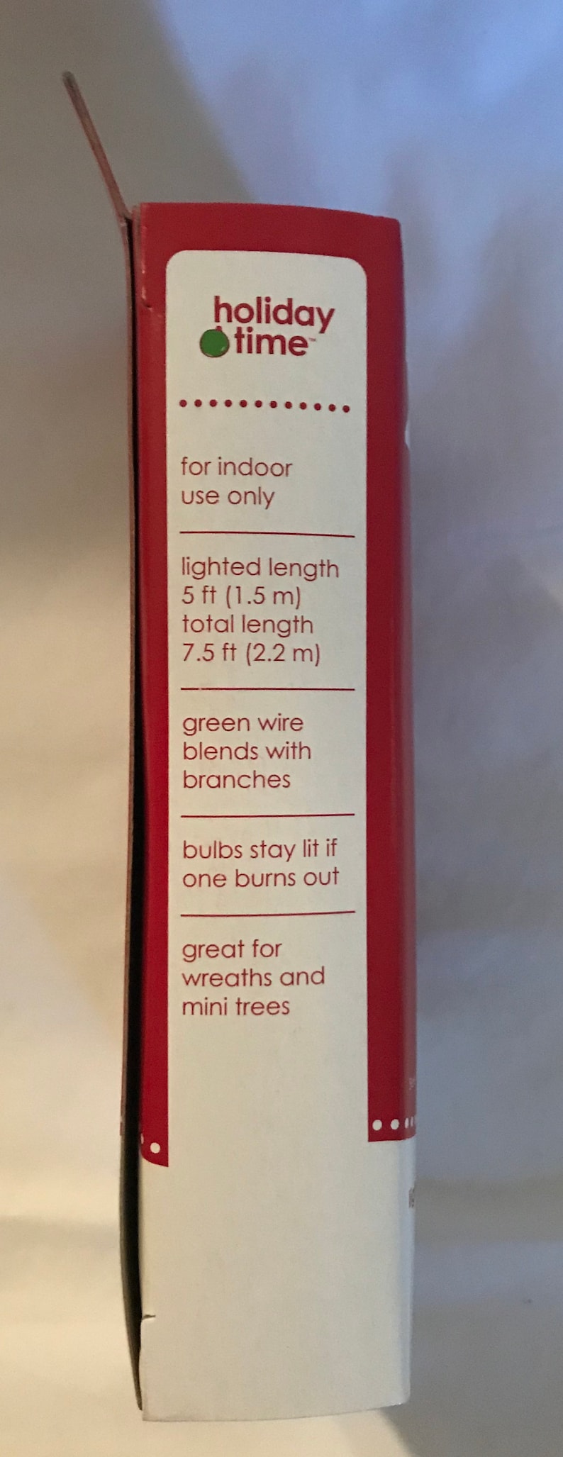 May include: A red and white box with the words "holiday time" and information about a 7.5 ft (2.2 m) long string of lights. The lights are designed to blend with branches and have green wire. The box says the lights are great for wreaths and mini trees.