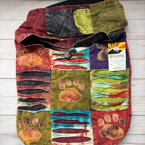 May include: A patchwork shoulder bag with a variety of colors including red, green, blue, and purple. The bag features paw print designs and a Rising tag. The bag has a button closure and a long strap.