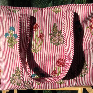 May include: A large, quilted tote bag with a pink and white striped pattern. The bag features embroidered floral designs in shades of blue, pink, and green. The bag has two handles and is made of a soft, textured fabric.