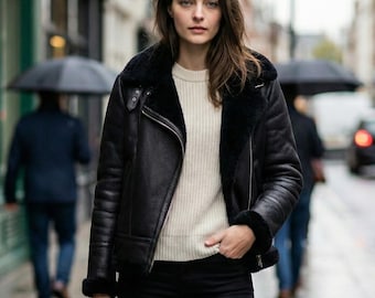 May include: A black leather jacket with a black faux fur lining, a cream-colored ribbed sweater, black skinny jeans, and a black structured handbag. The jacket features a wide collar, silver-tone zippers, and long sleeves with fur cuffs.