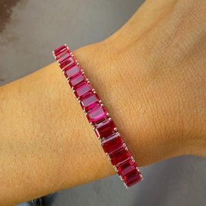 May include: A silver bracelet featuring rectangular, vibrant red gemstones. The gemstones are set closely together, creating a continuous band of color. The bracelet is shown on a wrist, highlighting its design and color.