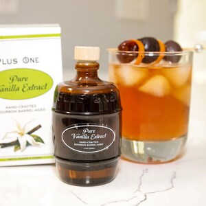 May include: A bottle of Pure Vanilla Extract, with a box and a cocktail. The extract bottle is brown with a wooden cap. The box is white with green text. The cocktail is in a clear glass with ice and a garnish.
