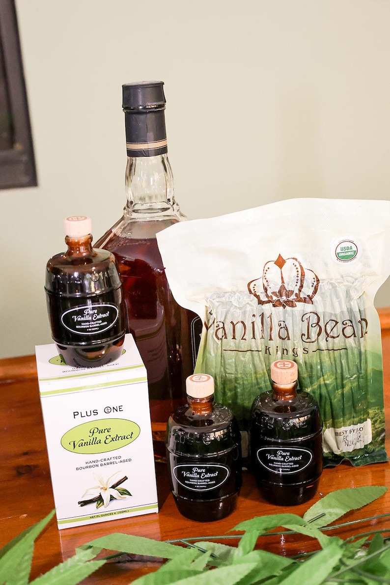 May include: A collection of vanilla products, including bottles of pure vanilla extract and a bag of vanilla beans. The extract bottles have a dark label and a wooden cap. A box of vanilla extract is also present.