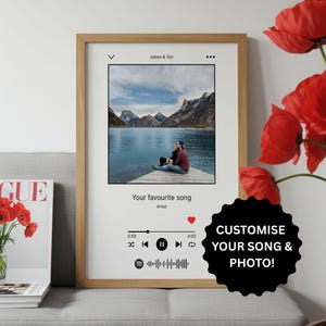 May include: A framed print with a wooden frame featuring a photo of a couple by a lake. The print includes a music player interface with the text "Your favourite song" and "Artist". A black sticker says "CUSTOMISE YOUR SONG & PHOTO!"