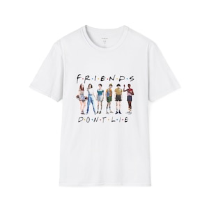 May include: White t-shirt featuring the text "FRIENDS DON'T LIE" in black, with a graphic of six characters. The design is a parody of the Friends TV show logo. The shirt is made of a soft material.