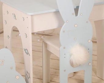 May include: A light blue and white children's table and chair set. The chair back is shaped like a bunny with a fluffy white tail. The table and chair are decorated with star and planet designs.