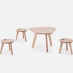 Puede incluir: Una mesa de madera clara y tres taburetes a juego. La mesa tiene una forma única y multifacética. Los taburetes son redondos con un pequeño asa recortada en la parte superior. Todas las piezas tienen tres patas anguladas.