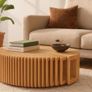 May include: A round coffee table constructed from vertical light-toned wooden slats arranged in a repeating pattern. On the flat surface sits a stack of two books, one with a green cover and one white with the text CREATE NO MEINFUL, and a dark bowl.