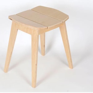 Op de afbeelding: Een lichtgekleurde houten kruk met een zitting van drie latten en schuine poten. De kruk heeft een eenvoudig, modern ontwerp en is gemaakt van natuurlijk hout. De poten zijn taps toelopend en de zitting heeft een unieke vorm.