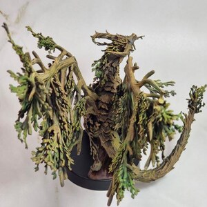 May include: A detailed sculpture of a dragon, crafted from wood and adorned with green foliage. The dragon has outstretched wings and a textured, bark-like appearance. It is mounted on a black base, showcasing the intricate details of the fantasy creature.
