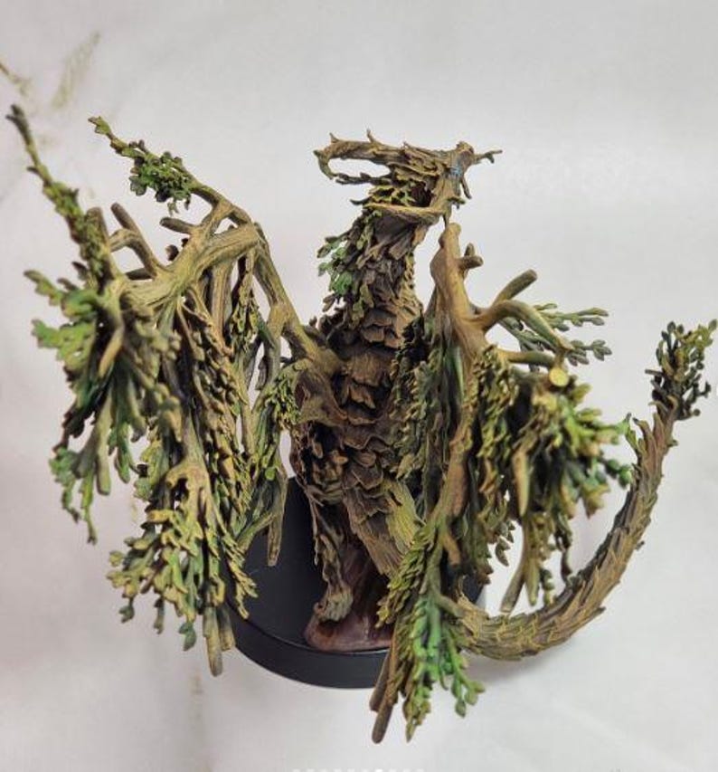 May include: A detailed sculpture of a dragon, crafted from wood and adorned with green foliage. The dragon has outstretched wings and a textured, bark-like appearance. It is mounted on a black base, showcasing the intricate details of the fantasy creature.