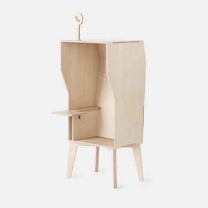 May include: A light-coloured wooden cabinet with a tall, narrow design. It features a small shelf, a lower storage area, and a decorative element on top. The cabinet has a minimalist aesthetic with clean lines and a natural wood finish.