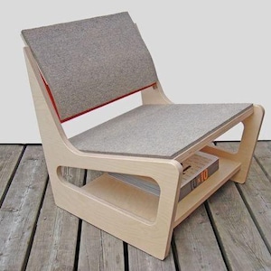 以下が含まれることがあります： 明るい灰色の座面と背もたれを備えたモダンな木製椅子。椅子は、本を置く棚が付いたユニークなデザインです。背もたれには赤いアクセントがあります。椅子は明るい色の木材で作られています。