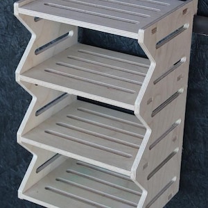 Puede incluir: Estantería de madera clara de cuatro niveles. Los estantes están soportados por un diseño en zigzag, con ranuras horizontales para ventilación. La unidad está hecha de madera contrachapada y es adecuada para el almacenamiento.