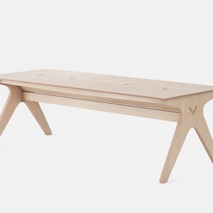 Può includere: Una panca in legno chiaro dal design minimalista. La panca ha un piano rettangolare con diversi piccoli ritagli distanziati. Le gambe sono angolate e divaricate, con un dettaglio a forma di V sui lati. La panca è realizzata in legno chiaro.