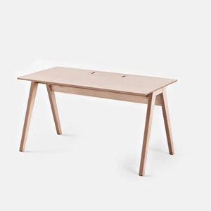 Puede incluir: Un escritorio de madera clara con una parte superior rectangular y patas anguladas. El escritorio tiene dos pequeñas aberturas cerca del borde trasero. El escritorio es de madera clara y tiene un diseño minimalista.
