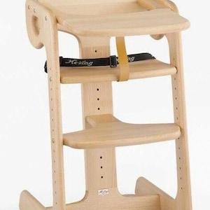 Peut inclure: Chaise haute en bois clair avec assise, repose-pieds et sangle de sécurité. Le design comprend un dossier et une base stable. Le nom de la marque "Herlag" est visible sur la sangle de sécurité. La chaise est réglable en hauteur.