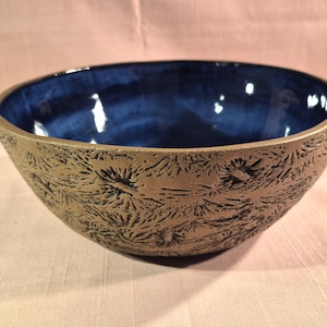 May include: A handmade ceramic bowl with a textured exterior and a deep blue interior. The bowl's exterior has a brown, rough surface with a repeating pattern. The interior is a glossy, dark blue color.
