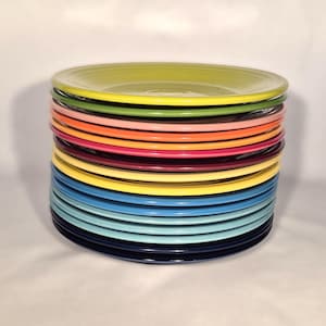May include: A stack of colorful ceramic plates in various shades, including yellow, green, pink, orange, red, blue, and navy. The plates are stacked neatly, showcasing a range of vibrant colors. These plates are perfect for adding a pop of color to any kitchen.