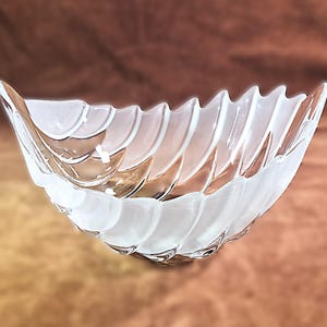 May include: A clear glass bowl with a frosted, wave-like design. The bowl has a curved shape and is likely used for decorative purposes or serving food. The frosted pattern adds a touch of elegance to the piece.
