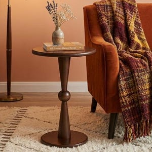 May include: A mid-century modern living room scene featuring a floor lamp with a beige shade, a small round side table, and an orange sofa with a plaid throw. A potted plant and a rug complete the cozy aesthetic.