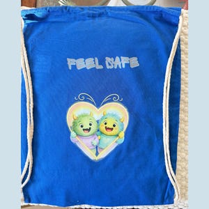 Könnte beinhalten: Ein blauer Kordelzugbeutel mit dem Text "FEEL SAFE" in Weiß. Die Tasche hat eine herzförmige Grafik mit zwei Cartoon-Monstern. Die Tasche hat weiße Kordelzüge.