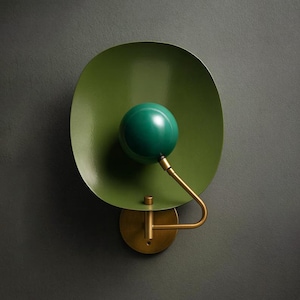 Könnte beinhalten: Moderne Wandleuchte mit grünem, scheibenförmigem Schirm und kugelförmigem grünem Licht. Sie hat einen messingfarbenen Arm und eine kreisförmige Messingbasis. Minimalistisches und stilvolles Design.