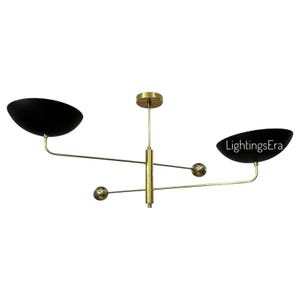 May include: A contemporary ceiling light with a mid-century aesthetic. It features two black, bowl-shaped shades and a brass-coloured frame. The design is minimalist, with a central vertical support and horizontal arms.