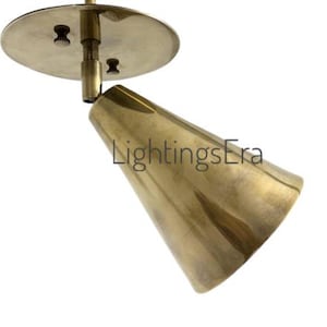 Könnte beinhalten: Ein kegelförmiger Strahler in Messingfarbe mit einer kreisförmigen Montageplatte. Die Leuchte ist nach unten abgewinkelt, und der Text "LightingsEra" ist auf der Seite sichtbar. Das Design ist minimalistisch und modern.