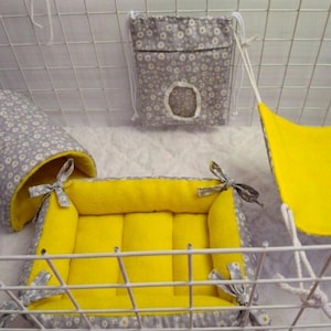 May include: A small animal bedding set featuring a grey and white floral print fabric with a bright yellow interior. The set includes a cylindrical tunnel, a square cushioned bed with corner ties, a hanging hammock, and a small drawstring pouch.
