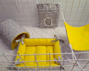 May include: A set of small animal bedding accessories including a gray tunnel with a white floral pattern and yellow interior, a rectangular yellow bed with gray floral edges, a yellow hammock, and a gray floral hanging pouch with a circular opening.