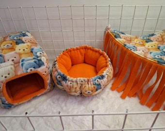 May include: A set of three small animal accessories including a cube-shaped hideout, a round bed, and a triangular hammock. Each piece features a fleece fabric with a colorful teddy bear pattern and bright orange interior lining and fringe.