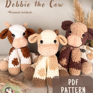 Puede incluir: Tres peluches de vaca de ganchillo hechos a mano en marrón, blanco y beige. Los peluches tienen orejas caídas y están sentados sobre una superficie rayada. El texto "Debbie the Cow" y "PDF PATTERN" son visibles.