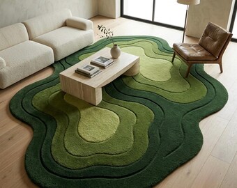 Può includere: Un tappeto dalla forma organica irregolare caratterizzato da strati concentrici e ondulati in varie tonalità di verde, che spaziano dal verde lime chiaro al verde bosco intenso, creando un effetto topografico su un pavimento in legno chiaro.