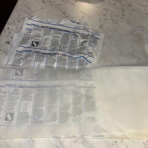 May include: A white, semi-transparent fusible interfacing sheet featuring printed instructional text and diagrams from HTC. The material is thin and lightweight, with a smooth texture on one side and a slightly textured adhesive surface on the other.