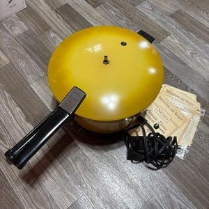 May include: A vintage yellow Sears Automatic Electric Pressure Cooker with a black handle and power cord. Includes the original instructions and recipe booklet. The pressure cooker has a round shape.