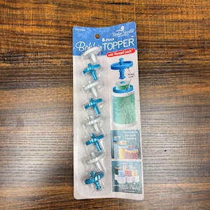 Puede incluir: Un juego de 8 piezas Taylor Seville Originals Bobbin Topper con Thread Lock en plástico azul y blanco. El empaque muestra el nombre del producto, instrucciones de uso en un carrete e imágenes que muestran la compatibilidad con varios carretes.
