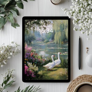 May include: A black tablet displays a serene landscape painting of a pond with two white geese. The time 16:34 is visible. The tablet is surrounded by white flowers, green leaves, a black stylus, and a white mouse on a white surface.