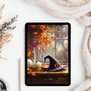 May include: A black tablet displaying a digital illustration of a purple witch hat, white pumpkins, and autumn foliage on a window sill. The screen shows the time 16:34 and the date Monday, June 18 in white text against the colorful fall scene.