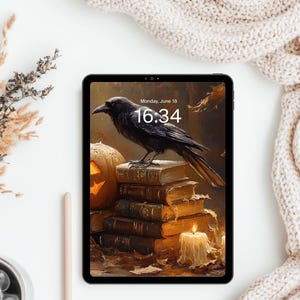 May include: A black tablet displaying a digital wallpaper of a crow perched on a stack of old books next to a glowing jack-o'-lantern and a lit candle, with the text "Monday, June 18" and "16:34" visible on the screen.