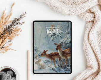 Pode incluir: Um tablet preto exibe uma cena de inverno com veados e um coelho em uma floresta nevada. A hora é 16:34 na segunda-feira, 18 de dezembro, com uma coruja acima. Uma xícara de café, uma caneta e plantas secas estão em uma superfície branca.