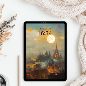 May include: A tablet displaying a digital wallpaper of a moonlit city with gothic architecture and warm glowing lights. The screen shows the text Monday, June 18 and 16:34. The device is positioned next to dried wheat stalks and a beige knit fabric.