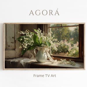 May include: A framed print featuring a still life of white lily of the valley flowers in a light blue pitcher with a ribbon. The image is set against a window with a view of a garden. The text "AGORÁ" and "Frame TV Art" are visible.