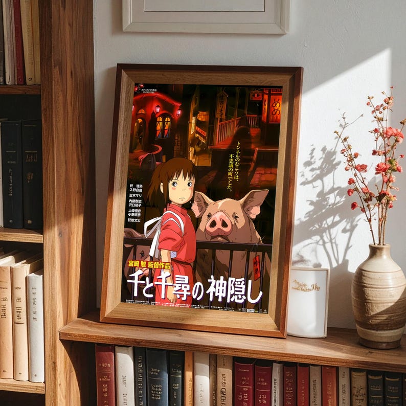May include: Framed poster featuring artwork from the animated film "Spirited Away." The poster shows a young girl in a red outfit with a pig, set against a backdrop of a nighttime street scene. Japanese text is visible.