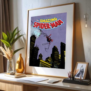 May include: Framed print of a vintage comic book cover featuring Spider-Man. The title "The Amazing Spider-Man" is displayed in red and white. Spider-Man is depicted swinging over a cityscape with a purple sky and a full moon.