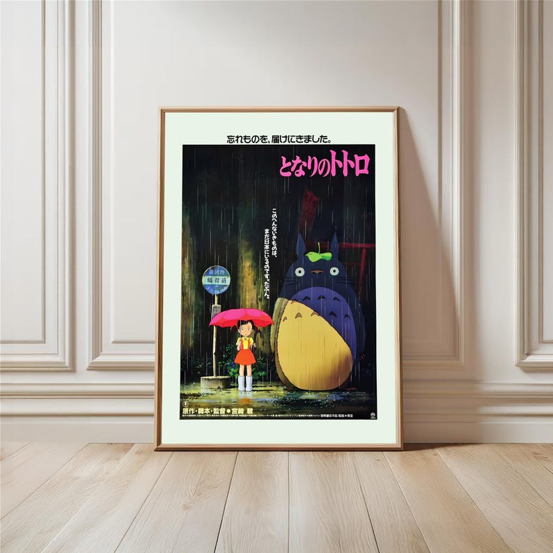 May include: Framed poster featuring a scene from the animated film "My Neighbor Totoro." The artwork depicts a young girl with a red umbrella standing at a bus stop in the rain, with Totoro nearby. Japanese text is visible.