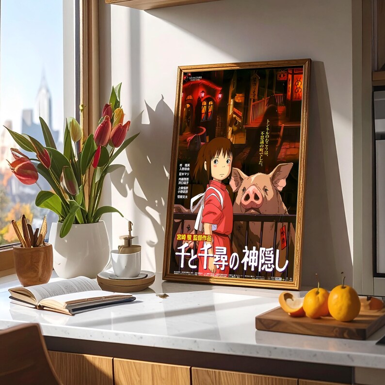 May include: A framed poster featuring the animated film "Spirited Away" with Japanese text. The poster shows a girl in a red outfit and a large pig. The poster is displayed on a white countertop next to a vase of tulips.