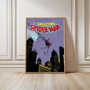 May include: A framed comic book art print featuring Spider-Man swinging through a city at night. The title "The Amazing Spider-Man" is displayed in bold, colorful lettering. The artwork has a vintage comic book style.