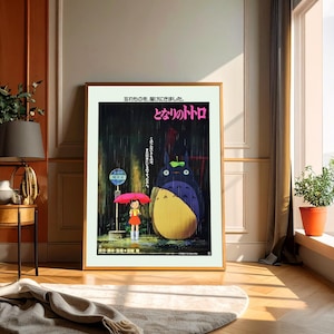 May include: Framed poster featuring the animated film "My Neighbor Totoro." The artwork depicts a young girl with a red umbrella standing at a bus stop in the rain, with Totoro, a large forest spirit, nearby. Japanese text is visible.
