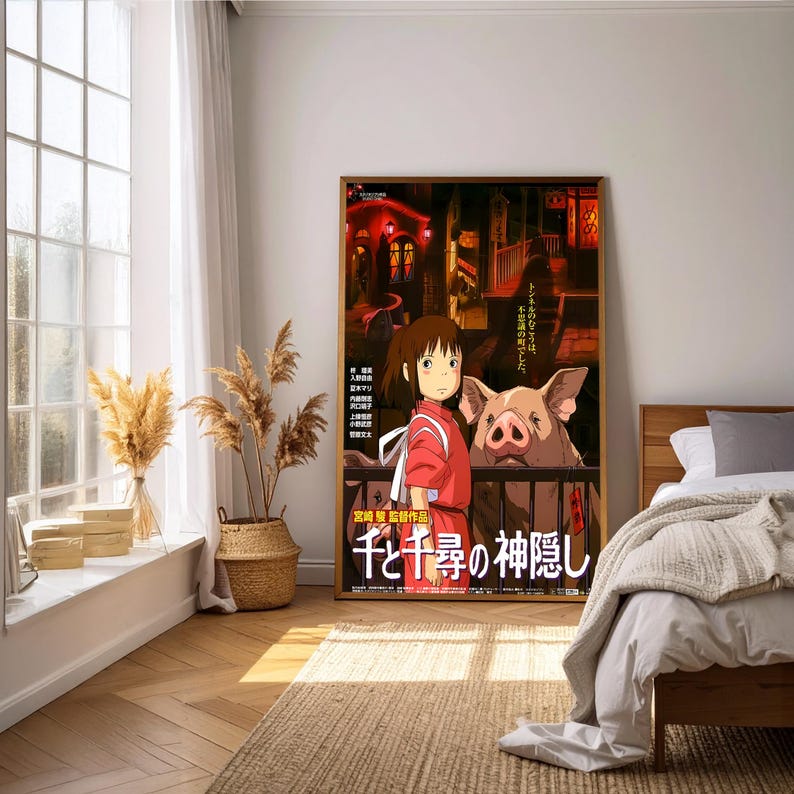 May include: A framed poster featuring artwork from the animated film "Spirited Away." The poster depicts a young girl in a red outfit and a large pig. Japanese text is visible at the bottom. The background shows a nighttime scene with buildings.